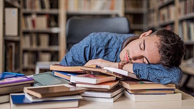 Student schläft in einer Bibliothek mit dem Kopf auf Büchern