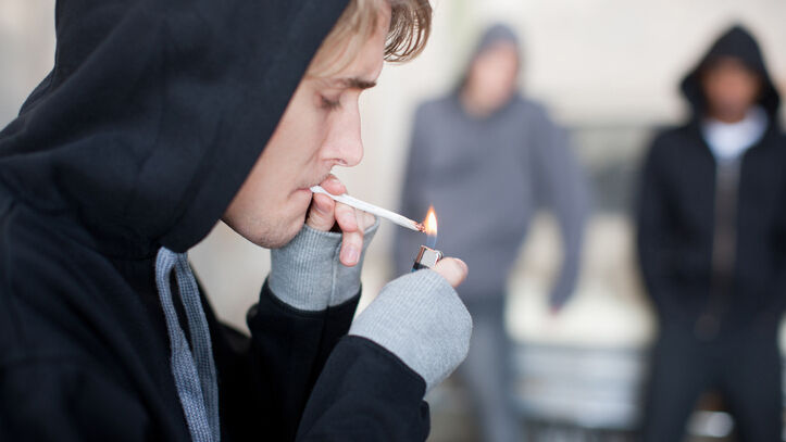 Junger Mann mit Kapuzenpulli zündet sich einen Joint an