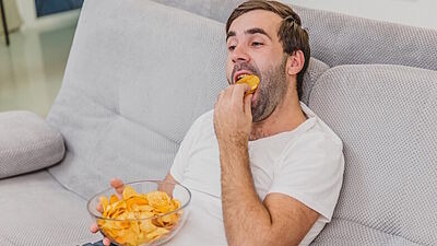 Mann sitzt auf Sofa und isst Kartoffelchips