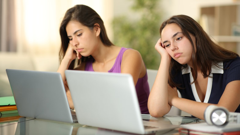 Zwei Studentinnen sitzen gelangweilt vor ihren Laptops