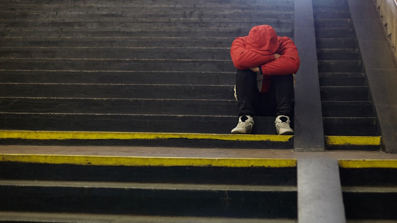 Junger Mann sitzt auf einer Treppe, sein Kopf liegt in seinen verschränkten Armen